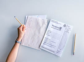 A top-down view of papers, exam booklets, and pencils on a clear tabletop
