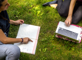 Two students sitting on the grass on their laptops